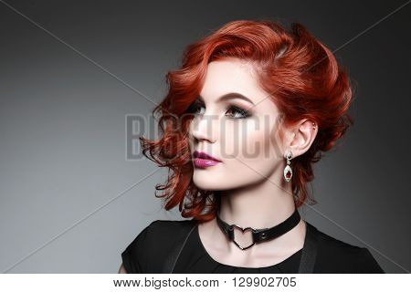 Portrait of beautiful woman with red hair and elegant hairstyle in black dress posing on gray background in studio. Fashion photo.