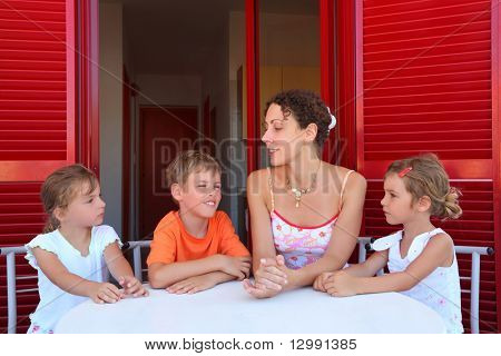 Трое детей и мать сидеть на веранде Круглая таблица возле двери и говорить