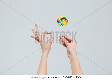 Coseup portrait of female hands holding lollipop and showing ok sign with fingers isolated on a white background