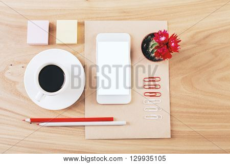 Top view of wooden desktop with blank white smartphone coffee cup cactus and stationery. Neatly organized. Mock up