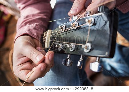 a man in a plaid shirt pulls in new guitar strings acoustic guitar close-up