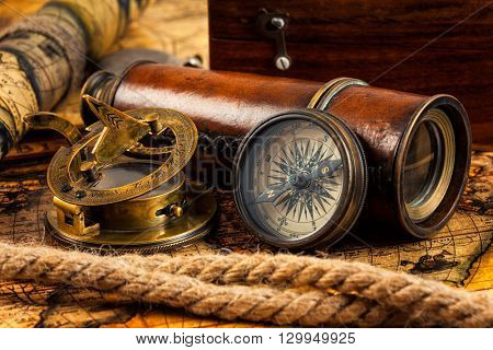 Travel geography navigation concept background - old vintage retro compass with sundial, spyglass and rope on ancient world map