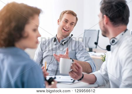 Exchange your ideas. Pleasant delighted positive colleagues sitting at the table and talking while woman working in the office