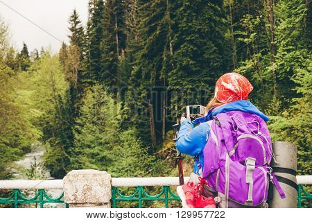 Young woman Traveler with a backpack taking a photo with smart phone mountain lake. Caucasus Abkhazia Lake Riza. Hiking Travel Lifestyle concept summer vacations outdoor.