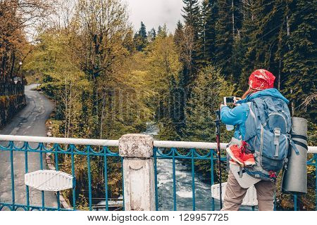 Young woman Traveler with a backpack taking a photo with smart phone mountain lake. Caucasus Abkhazia Lake Riza. Hiking Travel Lifestyle concept summer vacations outdoor.