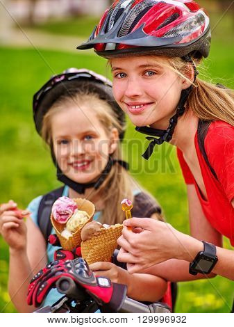 Bikes bicyclist girl. Portrait of girls wearing bicycle helmet with rucksack rides bicycle. Girls children are bicycling in summer park. Happy girls biking eating ice cream cone . 
