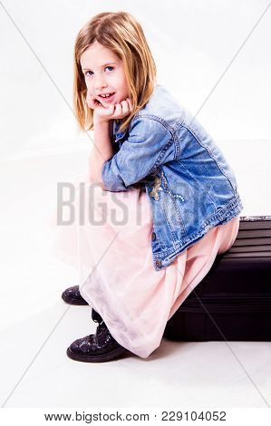 Portrait of a sweet little girl is sitting and thinking on a suitcase. Isolated on white background. Studio shot.