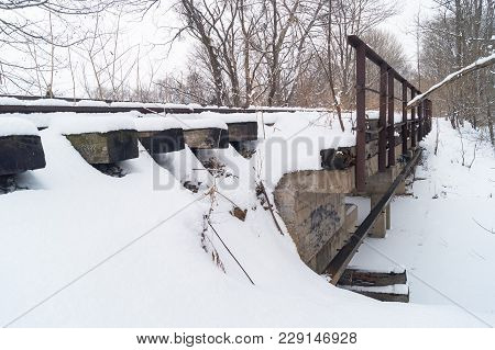 The Bridge To The Old Lost Railway In A Wild Place In The Winter Forest, Overgrown With Grass And Sh
