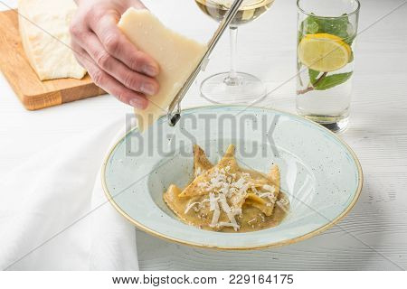A Chief Cook Masterly Preparing Delicious Green Ravioli. Cook's Hand Grates Parmesan On A Grater