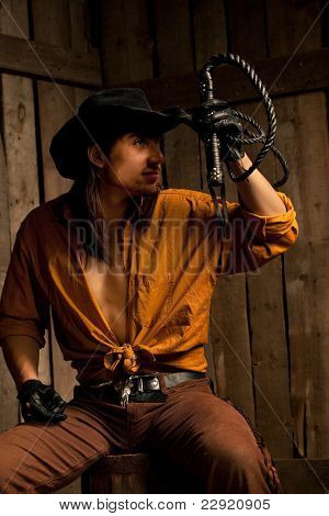 Cowboy with Black Leather Flogging Whip in his hand against wooden background