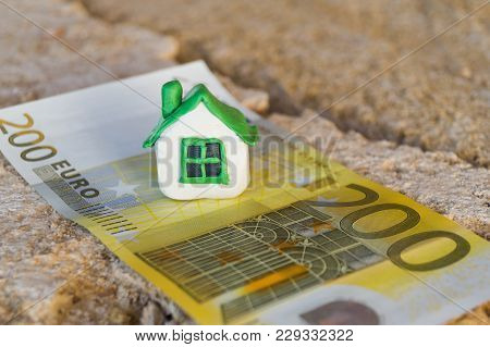 Small Miniature White Toy House With Green Roof Stands On The Banknote Of Euro Lying On A Beige Coqu