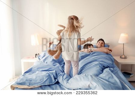 Cute awaken girl playing near sleeping family on bed at home