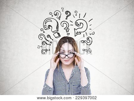 Attractive And Serious Asian Businesswoman Wearing A Striped Shirt Is Touching Her Glasses And Looki