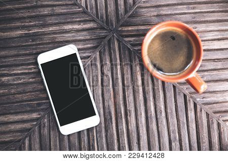Top View Mockup Image Of A White Mobile Phone With Blank Black Desktop Screen And A Cup Of Coffee On