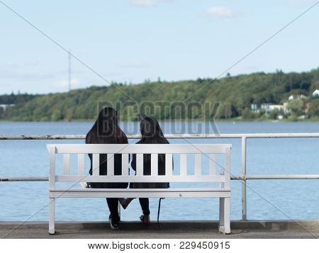 Two Girls Sitting On A Beach In Viborg, Denmark