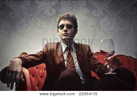 Hombre joven elegante sentado en un sofá de terciopelo y sosteniendo una copa de vino