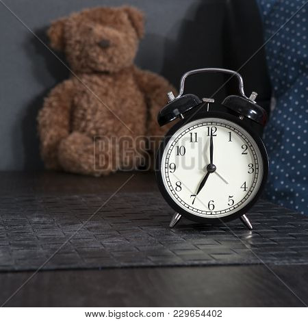 Black Alarm Clock On A Black And White Striped Napkin Showing 7 O'clock On A Bedside Table
