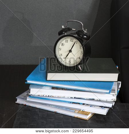 Black Alarm Clock On A Black And White Striped Napkin Showing 7 O'clock On A Bedside Table