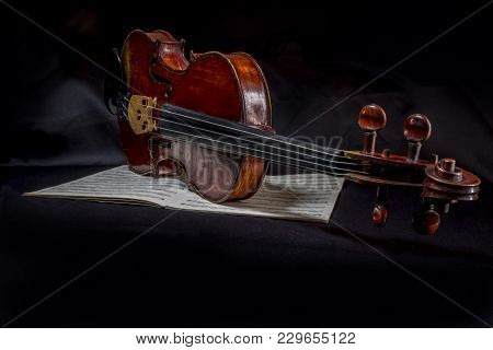 Family Heirloom. Antique Hand Made Violin Resting On Music Book Against Black Cloth Background. Musi