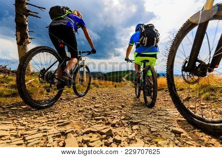 Mountain biking women and man riding on bikes at sunset mountains forest landscape. Couple cycling MTB enduro flow trail track. Outdoor sport activity.
