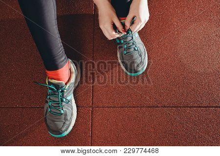 Close-up Of Girl Tying Shoelaces On Sports Shoes In Gym. Top View