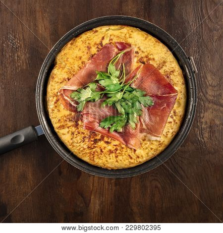 An Overhead Square Photo Of A Spanish Tortilla In A Traditional Tortillera, With Jamon And Parsley, 