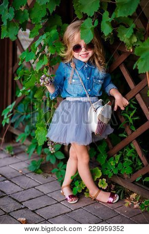 Little Girl In Jeans Shirt And Sunglasses Posing And Smiling.
