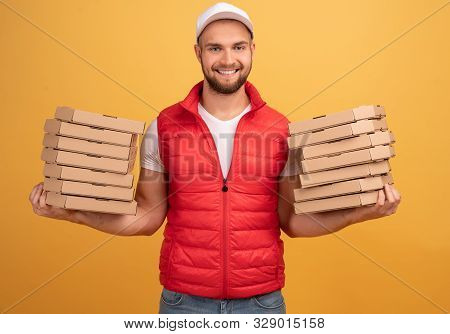 Horizontal Shot Of Happy Man Holds Two Piles Of Carton Boxes With Pizza, Has Surprised Joyful Expres