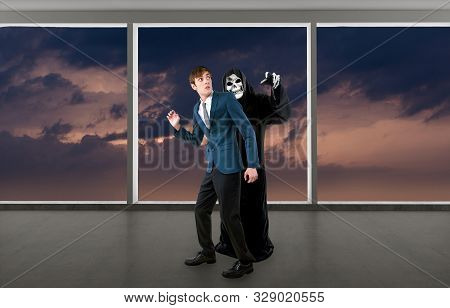 Man In A Halloween Grim Reaper Ghost Costume Chasing, Mocking And Making Fun Of Scared Businessman R