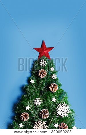 Christmas tree made of natural spruce branches deecor with red star on blue background, flat lay card with copy space