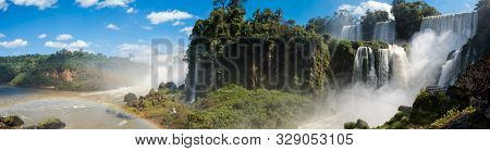 A Panoramic Of The Famous Iguazu Falls With Many Waterfalls Gushing Water On The A Sunny Day.