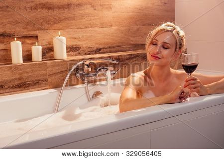 Lonely Sexy Blonde Single Woman Drinking Red Wine In Bath With Foam Next To The Candle Fire