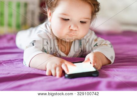 Harm From A Mobile Device To A Child. Toddler Boy Is Lying Looking At The Phone. The Concept Of Depe