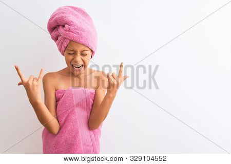 Beautiful child girl wearing shower towel after bath standing over isolated white background shouting with crazy expression doing rock symbol with hands up. Music star. Heavy concept.