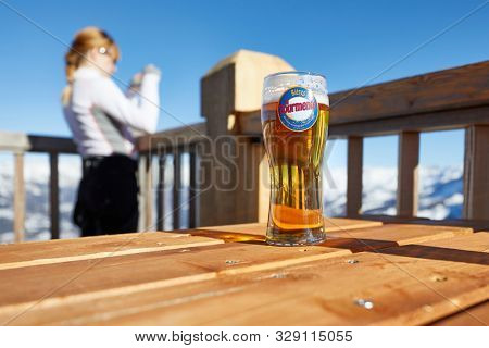 VAL D'ALLOS, FRANCE - JANUARY 23, 2018: Having a glass of beer in the snowy mountains, woman taking pictures of the scenic landscape view of the Alps. Beer from La Tourmente brewery in France