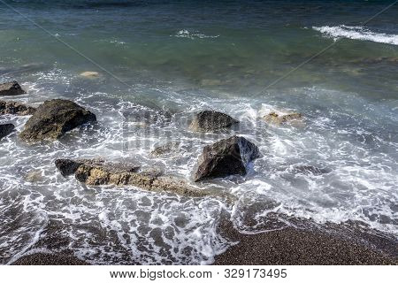 Sea Surf On The Beach With Black Volkanic Sand And Stones.