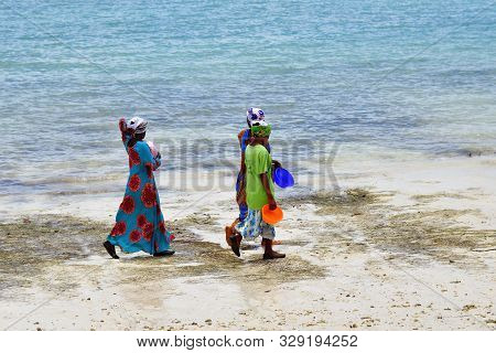 Kendwa, Zanzibar - October 3, 2019: Local Women In Traditional Dress Going Along The Ocean Shore Dur