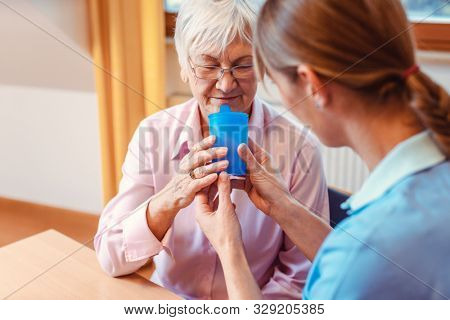 Caregiver helping senior woman drinking giving her a cup of water and holding it