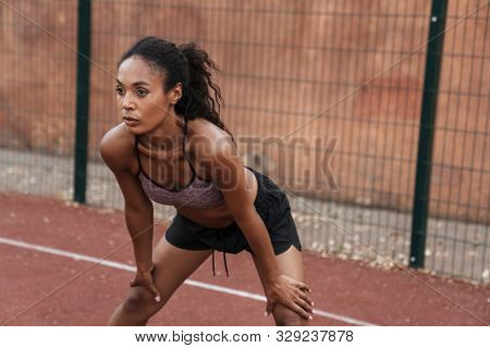 Image of concentated african american woman in sportswear doing workout at playground outdoors