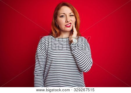 Young redhead woman wearing strapes navy shirt standing over red isolated background touching mouth with hand with painful expression because of toothache or dental illness on teeth. Dentist concept.