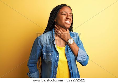 Young african american woman wearing denim shirt standing over isolated yellow background Touching painful neck, sore throat for flu, clod and infection