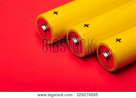 Close up shot of yellow AA alkaline or rechargeable NiMH batteries on red background, shallow focus