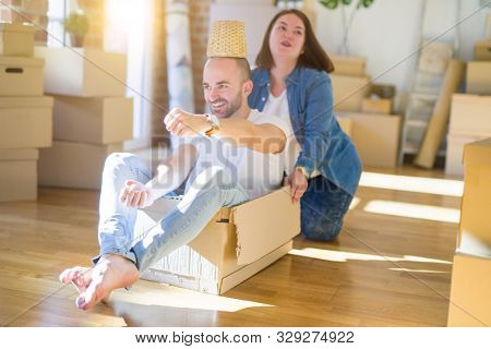Funny and crazy couple having fun riding a cardboad box as a car, smiling happy and lauging at new home