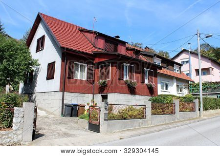 Attached Newly Built Wooden And Concrete Small Suburban Family House With Metal Fence And Flowers In
