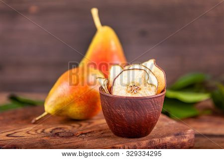 Close-up Of Sliced Homemade Dried Pears In Wooden Cup With Two Fresh Red Pears And Green Leaves Back