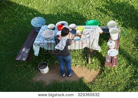 Woman Washes Up Dirty Dishes At Countryside Outdoors In Summer