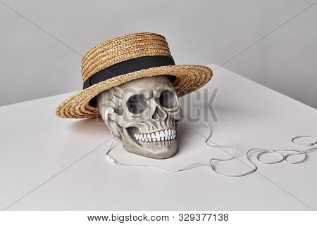 Realistic Model Of A Human Skull With Teeth In A Yellow Straw Hat And Headphones On A Light Table, W