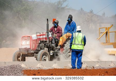African construction workers riding a tractor on a construction site, lots of dust, southern Africa, developing countries,