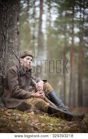 A Soldier Of World War Ii In Military Clothes Is Sitting In The Forest And Smoking