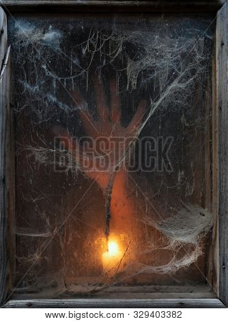 Terrible darkness. A spooky spider web in an old window. Hand of a ghost in the light of a candle